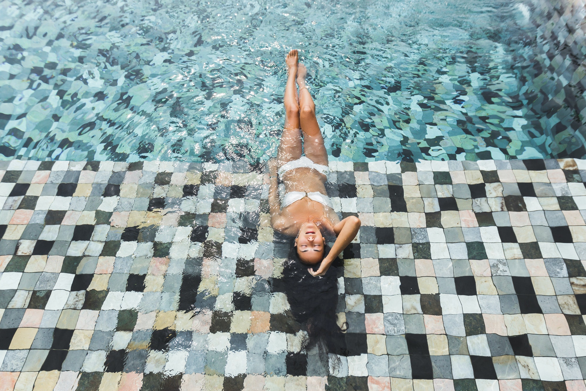 Woman relaxing in luxury swimming pool in white bikini